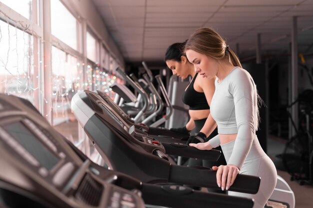 Side view of two attractive athletic women in the gym on a treadmill Girls on the treadmill