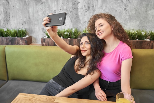 Side view of two best friends doing selfie in cafe