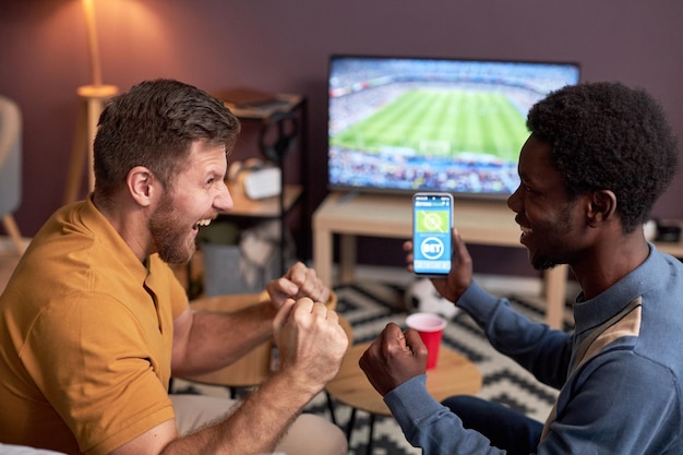 Photo side view two emotional football fans watching match at home and celebrating win