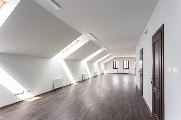Vista laterale dell'interno della stanza non ammobiliato con pavimento in legno su pareti bianche del pavimento del tetto con luce diurna luminosa