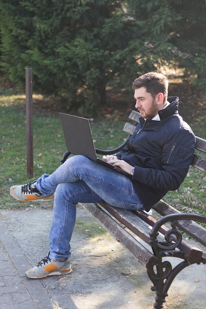 Side view van een jonge man die een laptop gebruikt terwijl hij op een bank zit