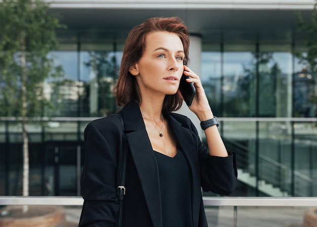 Side view van een mooie zakenvrouw die op een mobiele telefoon praat tegen een glazen gebouw
