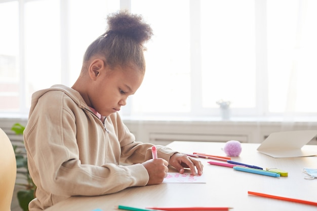 Side view view portrait of cute African-American girl signing handmade card as gift for Fathers day, copy space