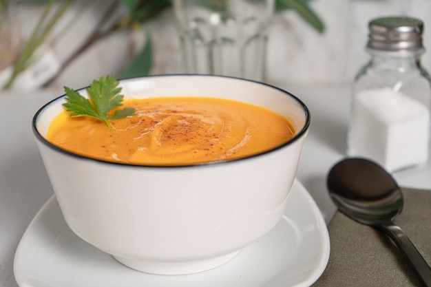 Side view of a white bowl with butternut squash and carrot cream soup