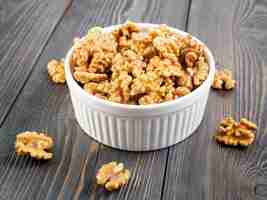 Photo side view white bowl with a handful of walnut circassian nuts on a wooden dark background