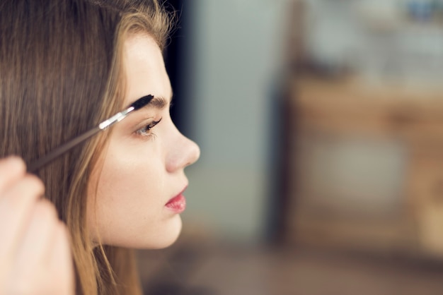 Photo side view woman applying makeup on eyebrows