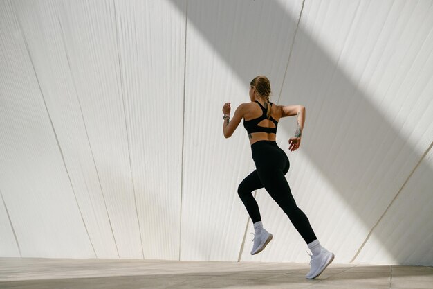 Photo side view of woman athlete is jogging on morning on modern building background healthy life concept
