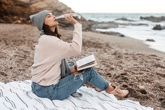 Foto vista laterale della donna in spiaggia a bere e leggere un libro