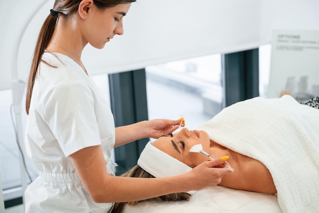 Vista laterale del viso di una donna che si fa la cura del viso con le mani di un estetista in un salone termale