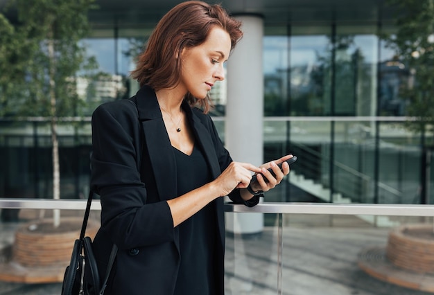 Side view of a woman in formal wear typing on a smartphone