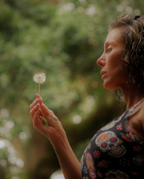 Photo side view of woman holding dandelion against trees