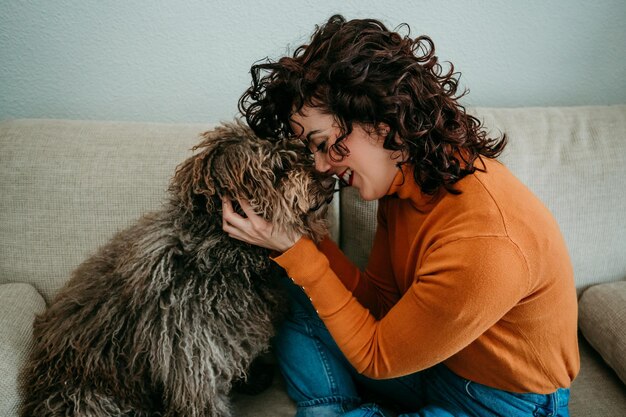 Photo side view of woman holding dog while sitting on sofa at home