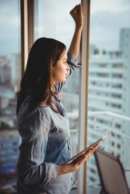 Side view of woman holding tablet while looking through window