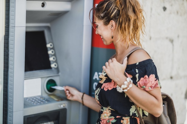 Side view of a woman inserting credit card and withdrawing cash at ATM machine.