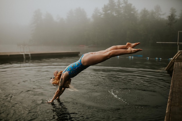 side view of woman jumping in lake during foggy weather