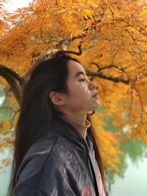 Side view of woman looking away while standing outdoors during autumn