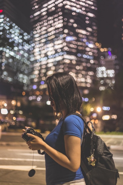 Photo side view of woman photographing in illuminated city at night