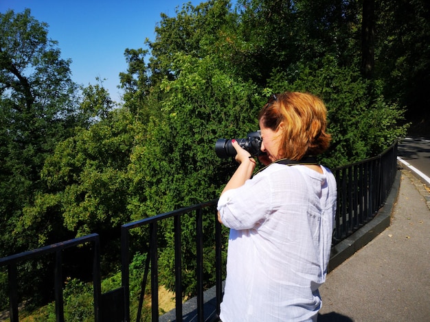 Foto vista laterale di una donna che fotografa gli alberi dalla strada