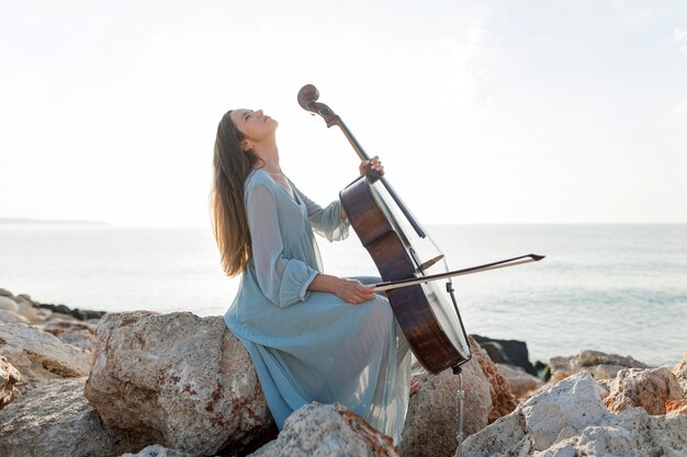 Foto vista laterale della donna che suona il violoncello in riva al mare