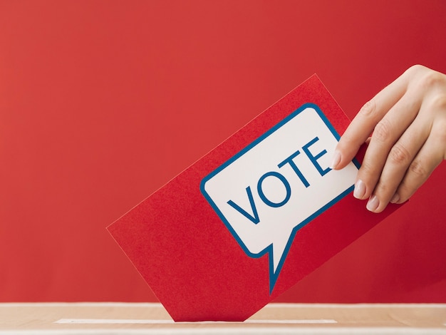 Side view woman putting a red voting card in a box 