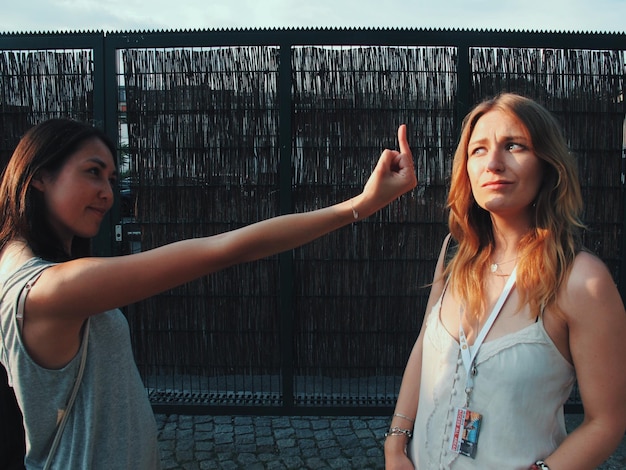 Photo side view of woman showing obscene gesture to her friend while standing outdoors