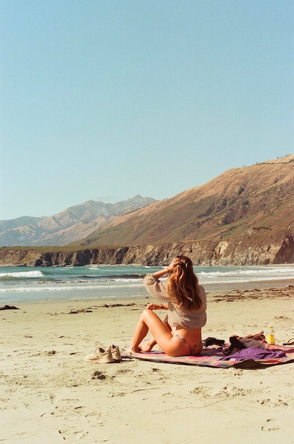 Side view of woman sitting at beach against clear sky