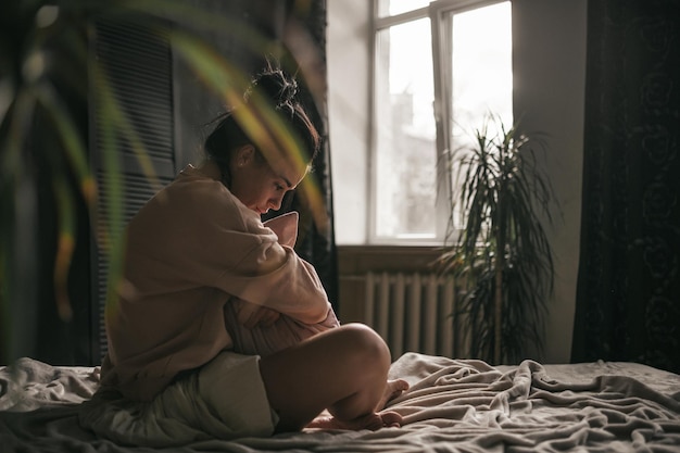 side view of woman sitting on bed at home