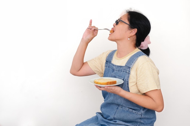 Photo side view of a woman sitting and biting her bread using fork for breakfast