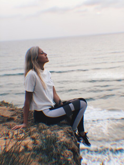 Foto vista laterale di una donna seduta sul mare su una roccia