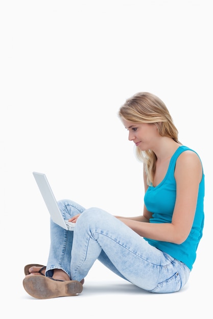 Photo a side view of a woman sitting on the ground typing on a laptop