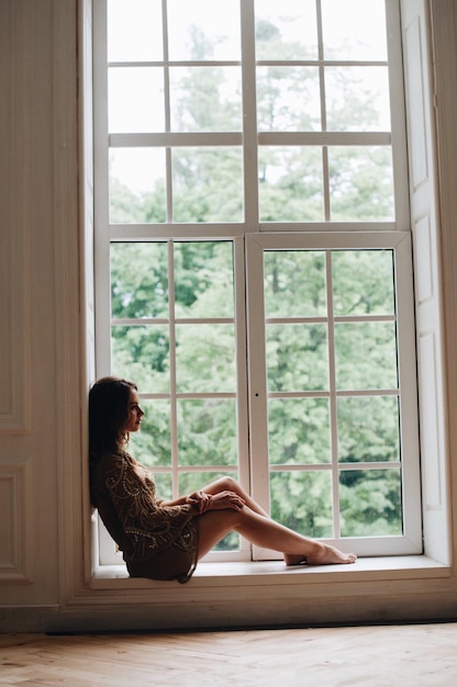 Foto vista laterale di una donna seduta sul davanzale della finestra a casa