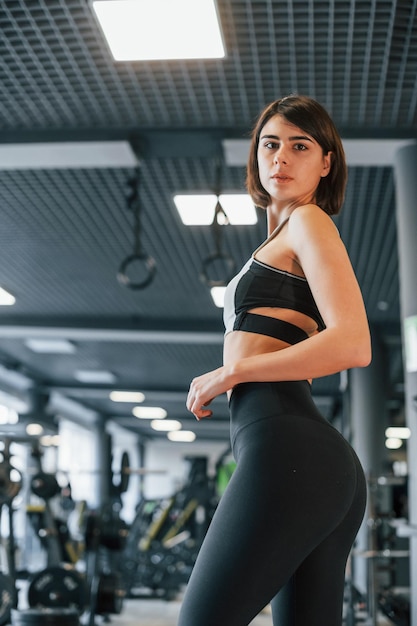 Photo side view woman in sportive clothes with slim body type is in the gym