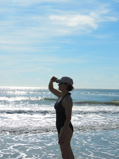 Photo side view of woman standing at beach against sky