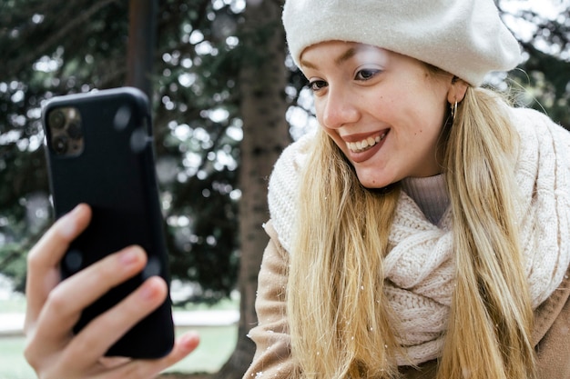 Vista laterale della donna che cattura selfie nel parco durante l'inverno