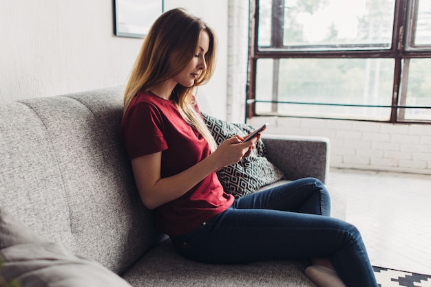 Side view of woman using mobile phone while sitting on sofa at home.