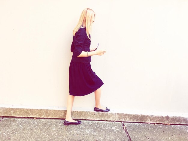 Photo side view of woman walking by wall