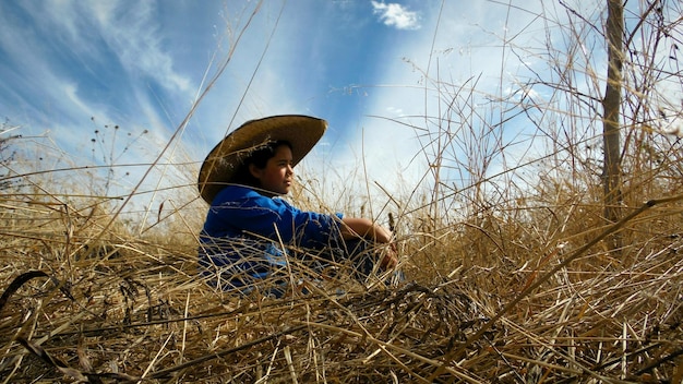 Side view of woman wearing hat sitting on grassy field against sky