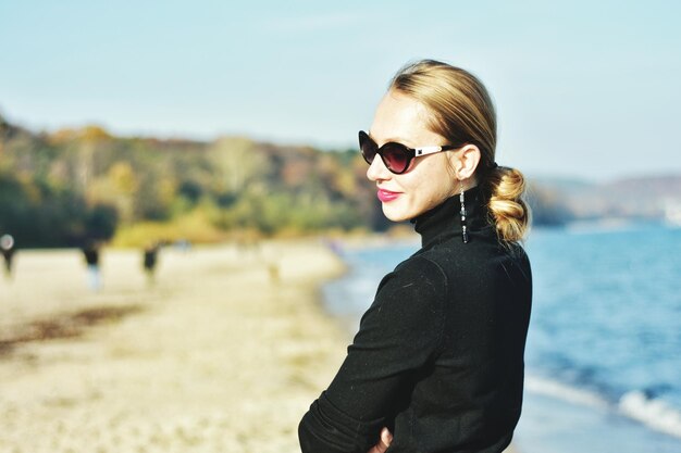 Side view of woman wearing sunglasses while standing at beach