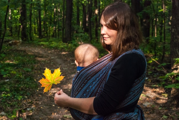 Foto vista laterale di una donna con un bambino che porta un tessuto nella foresta