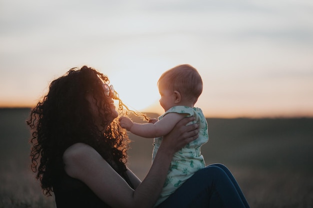 Foto vista laterale di una donna con un bambino seduta sul campo durante il tramonto