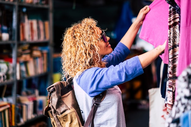 Photo side view of woman with backpack choosing cloth at market