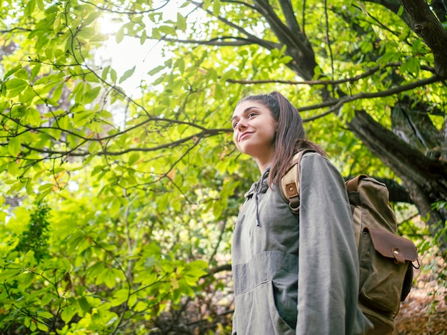 Side view of woman with backpack in the forest admiring the wild nature looking up with smile