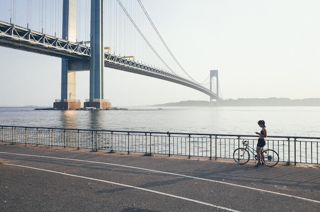夕暮れの空に向かって散歩道に立っている間スマートフォンを使って自転車に乗っている女性のサイドビュー