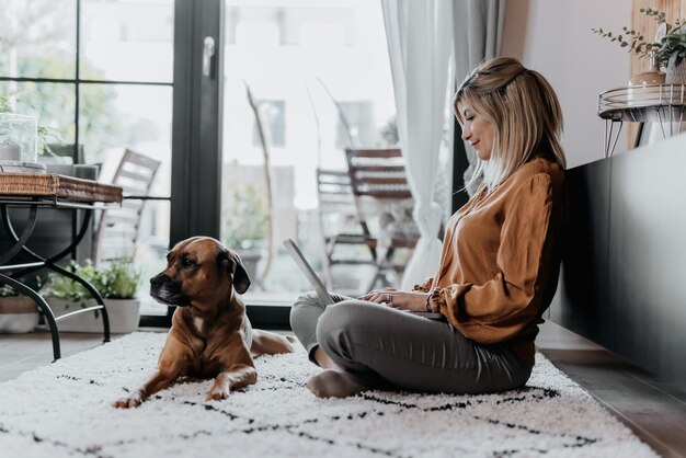 Photo side view of woman with dog sitting on floor at home