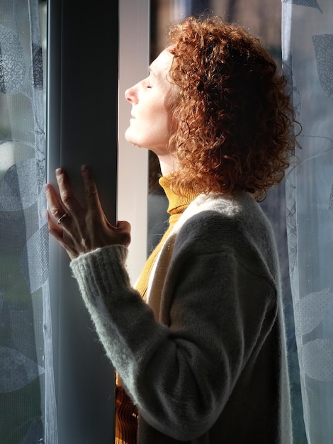 Foto vista laterale di una donna con gli occhi chiusi che fa il bagno di sole attraverso la finestra a casa