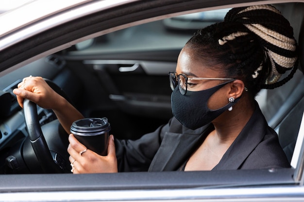 Foto vista laterale della donna con la maschera per il viso con caffè all'interno della sua auto