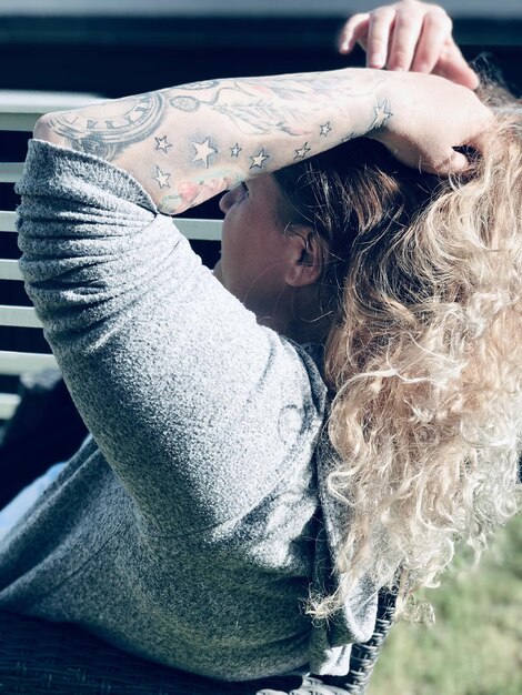 Боковой вид женщины с рукой в волосах, сидящей в парке