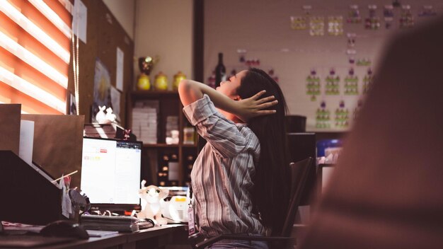 Photo side view of woman with hand in hair while working over computer at office