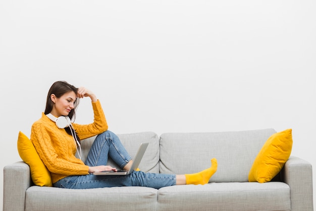 Foto vista laterale della donna con le cuffie che si siedono sul sofà con il computer portatile