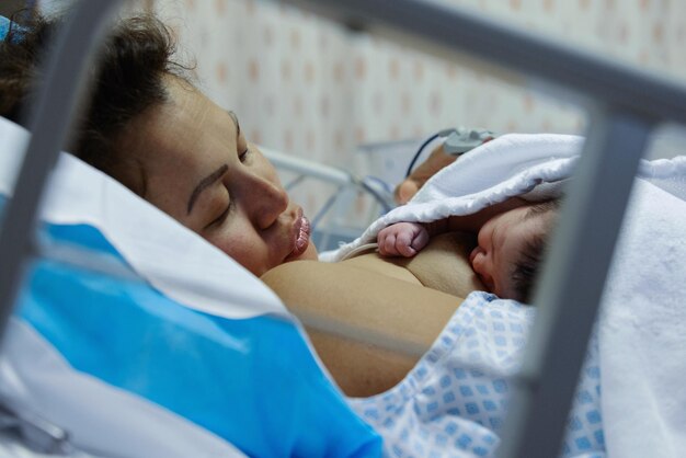 Photo side view of woman with new born on bed at hospital